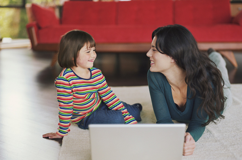 A parent on a laptop with her child.