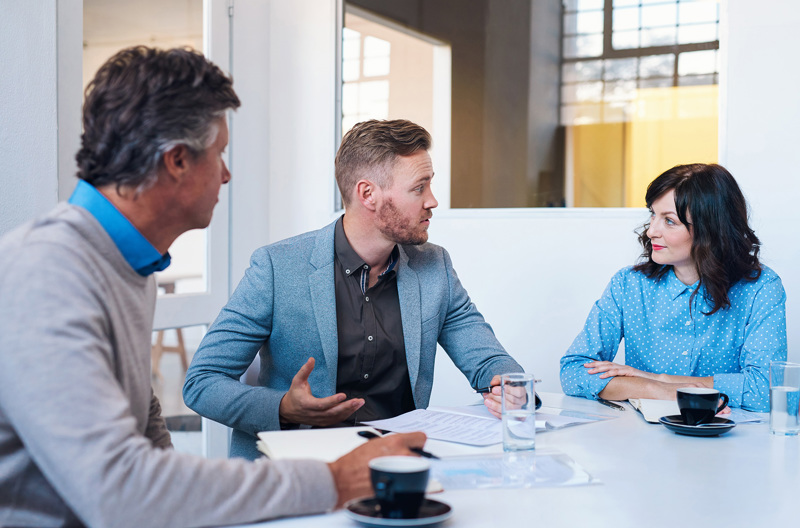 Three people sitting together at a table talking and writing notes. 