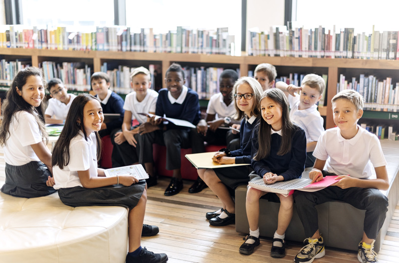 A group of school students sitting down on chairs in a library.