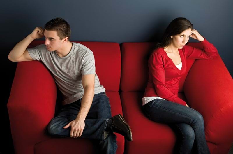 A couple sitting at opposite ends of a couch, looking away from each other.
