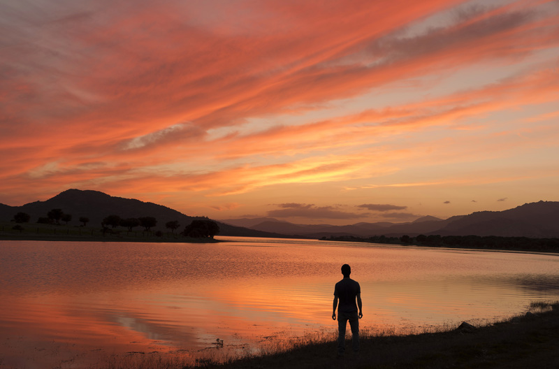 A person standing next to a large pool of water with a red sky in the background.