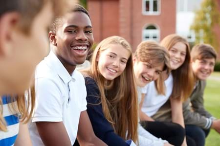 A group of teenagers sitting next to each other smiling.