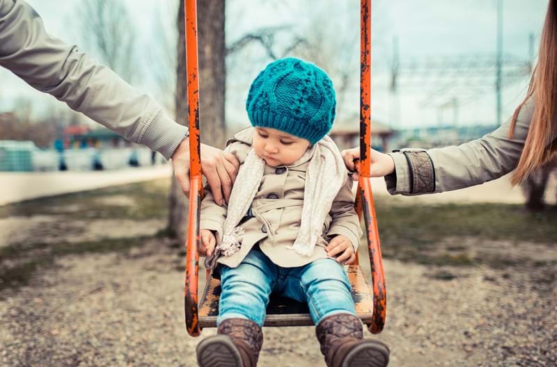 A child on a swing pushed by their parents. 