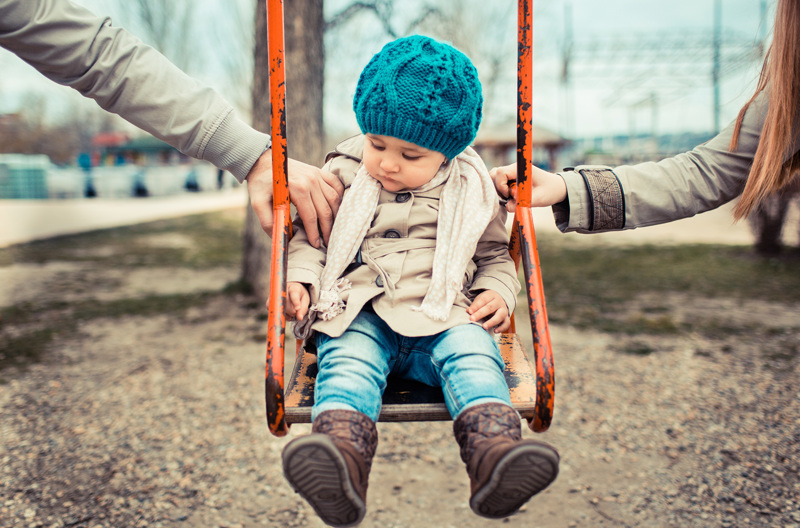 A child on a swing pushed by their parents. 