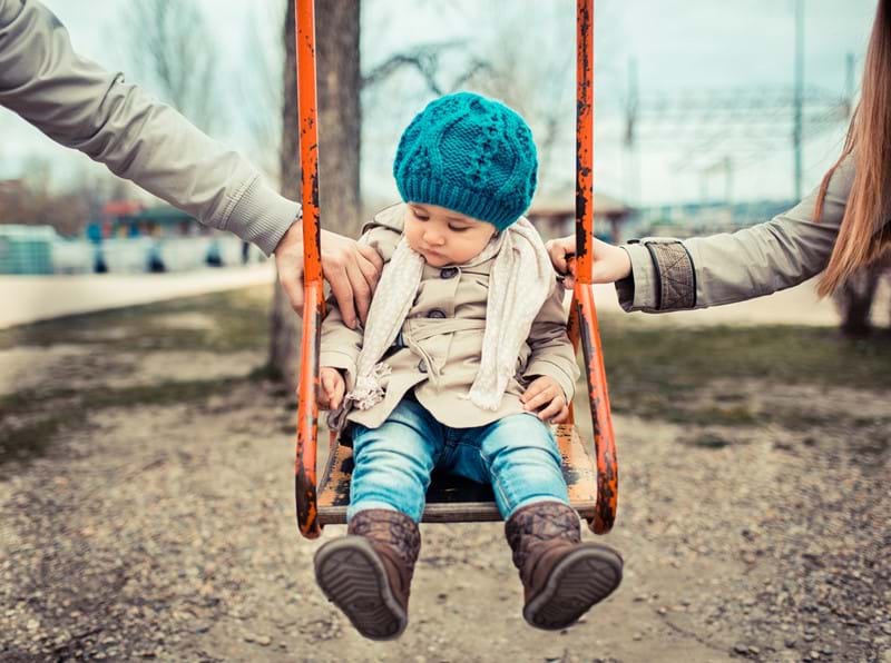 A child on a swing pushed by their parents. 