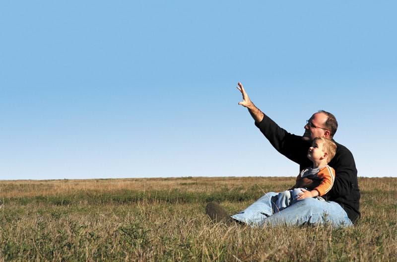 A parent pointing toward the sky with their child sitting in their lap.