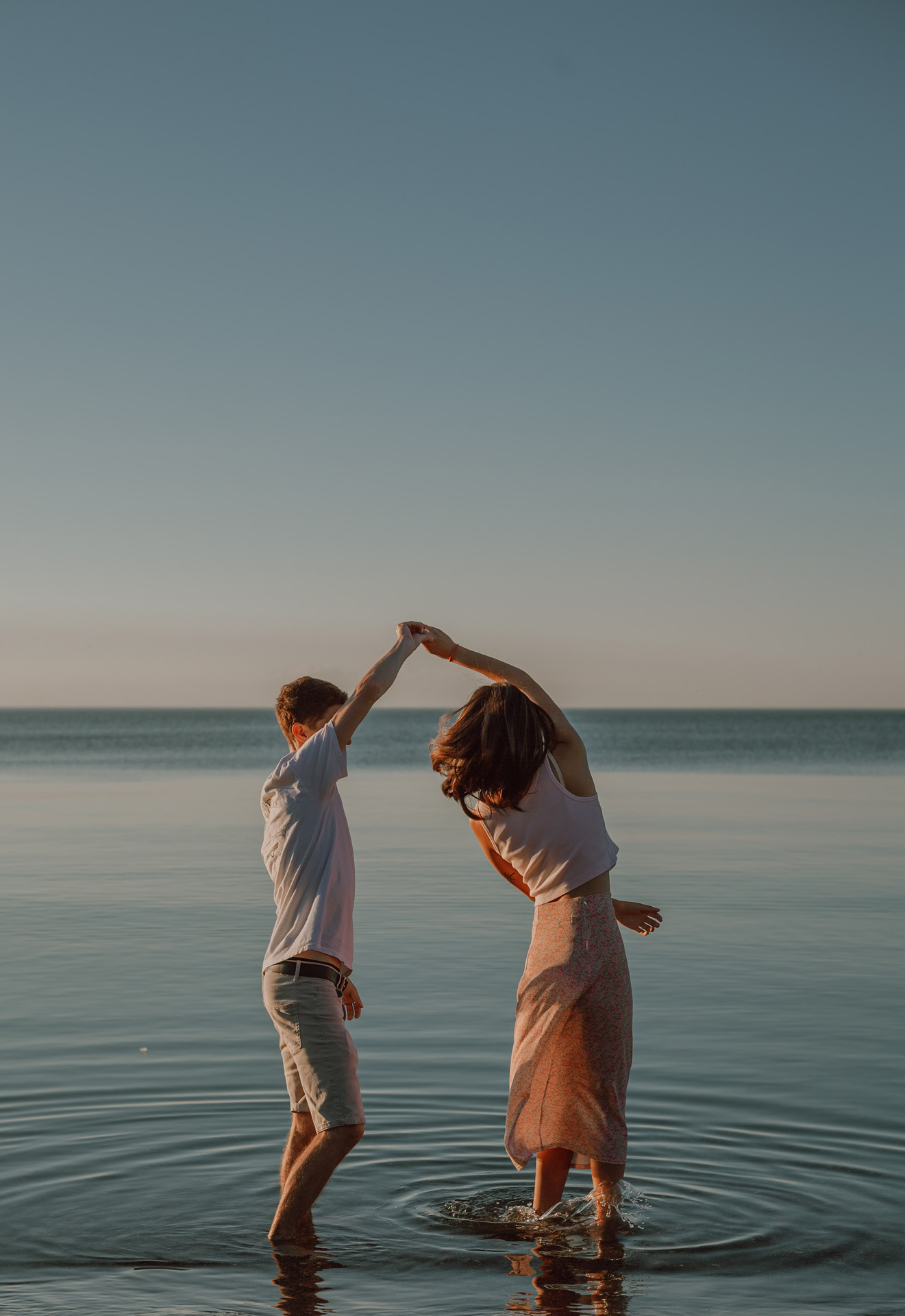 A couple standing in water holding holds while dancing. 