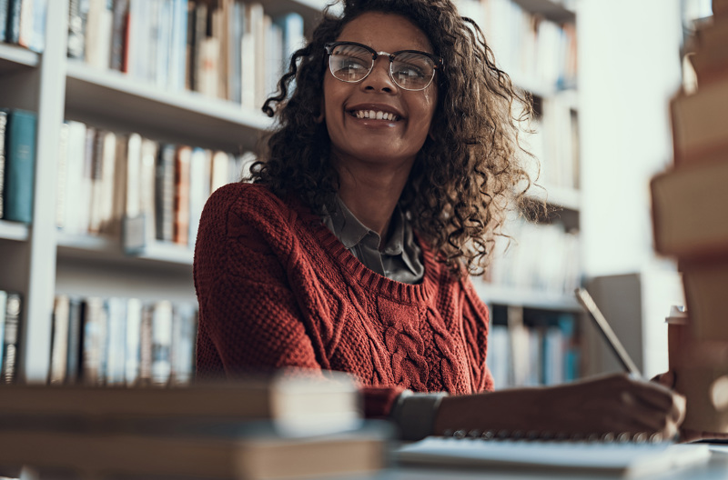 A woman sitting at a desk smiling while taking notes. 