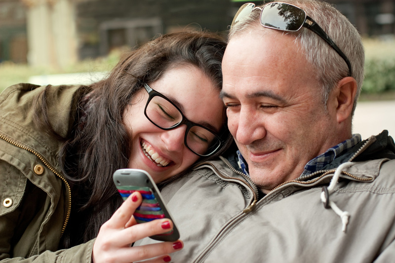 A smiling child showing her parent something on her phone.