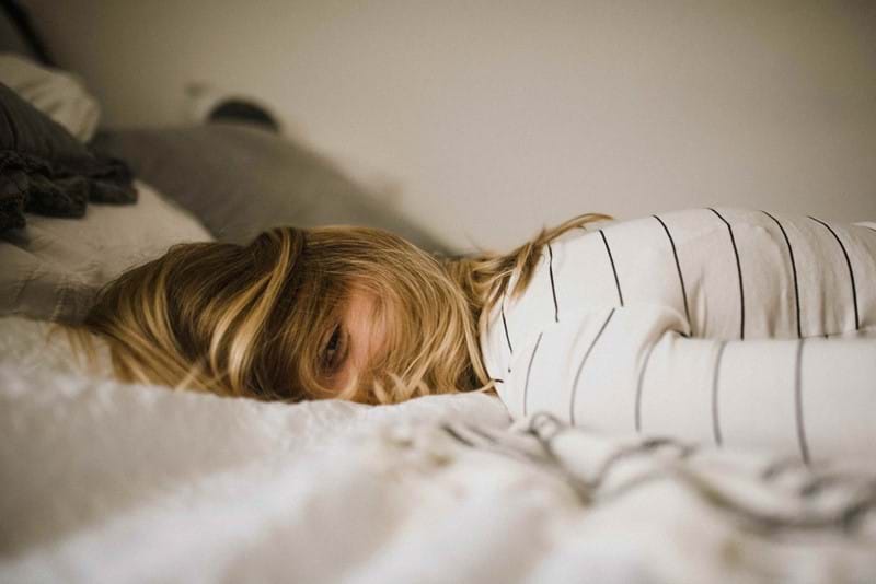 A blonde haired girl laying face down on a bed.