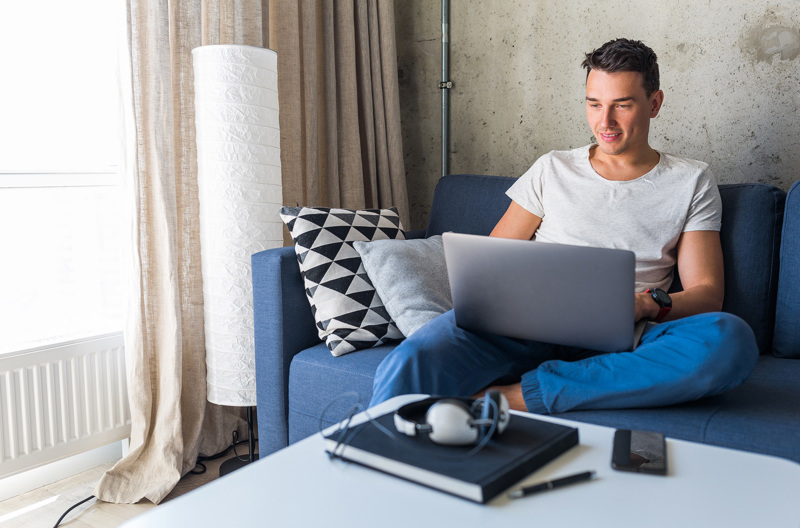 A man sitting down on a blue couch with an open laptop on his lap.