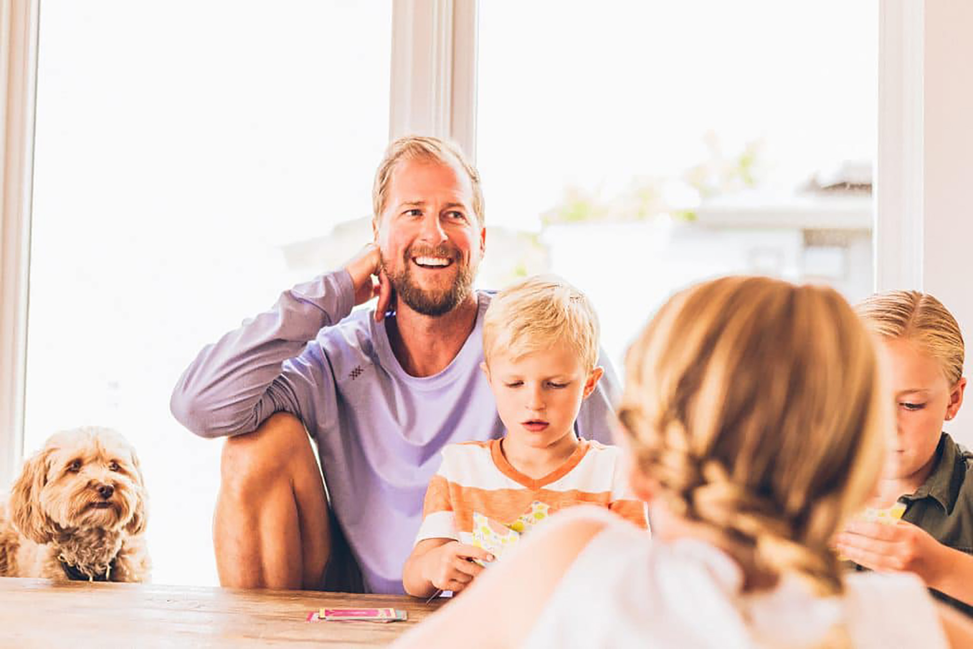 A dad sitting with his two children and a dog at a table.