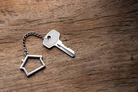 Key attached to a key ring shaped like a house on a timber surface.