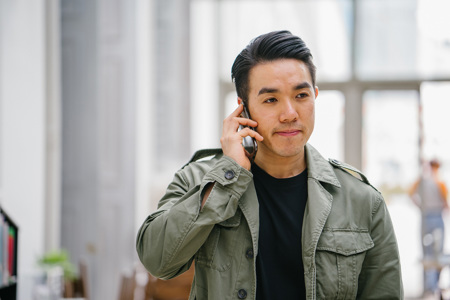 A man wearing a green shirt smiling while on the phone.