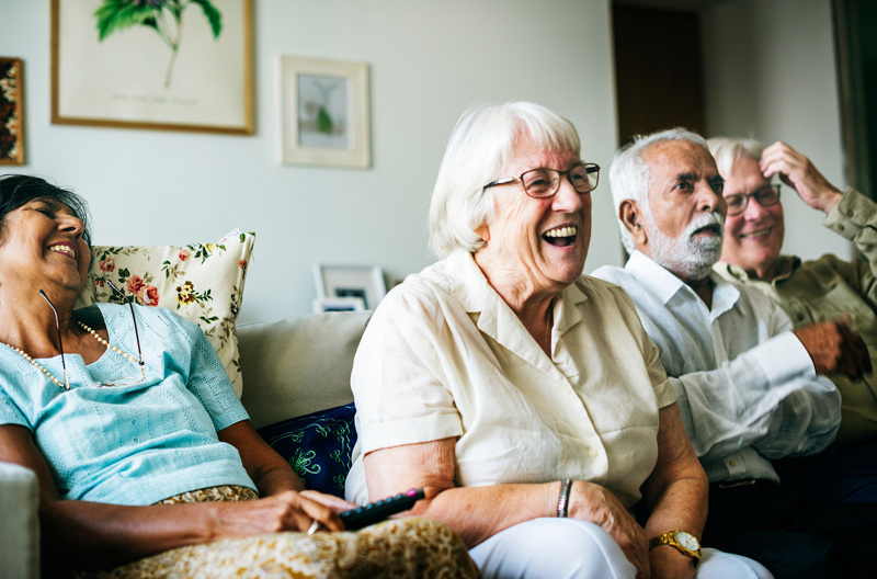 Four people sitting together on a couch laughing. 