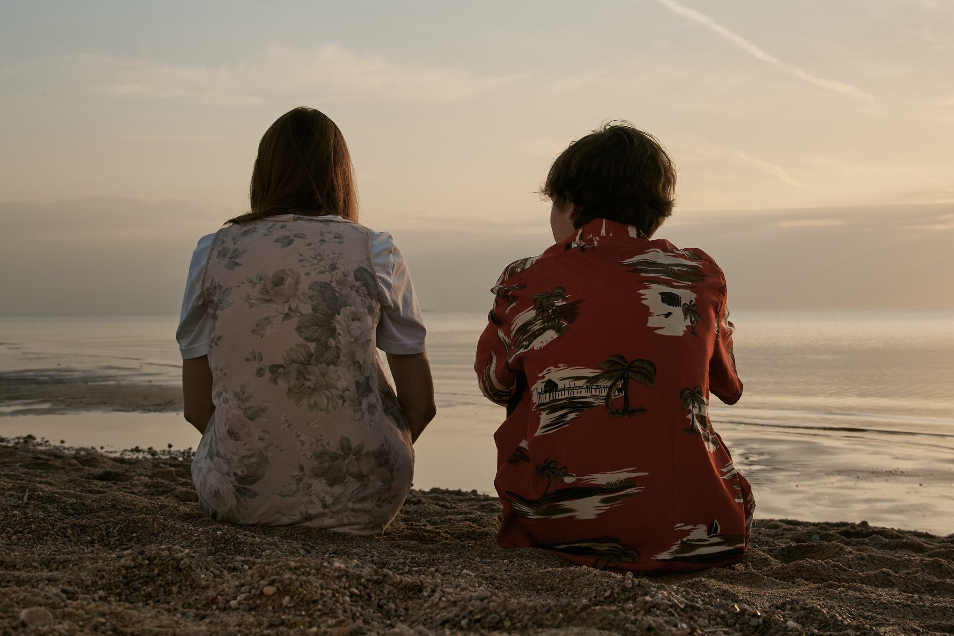 A couple sitting side by side on a hill overlooking the ocean. 