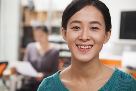 A young woman wearing a green top smiling at the camera while someone reads off a piece of paper in the background.
