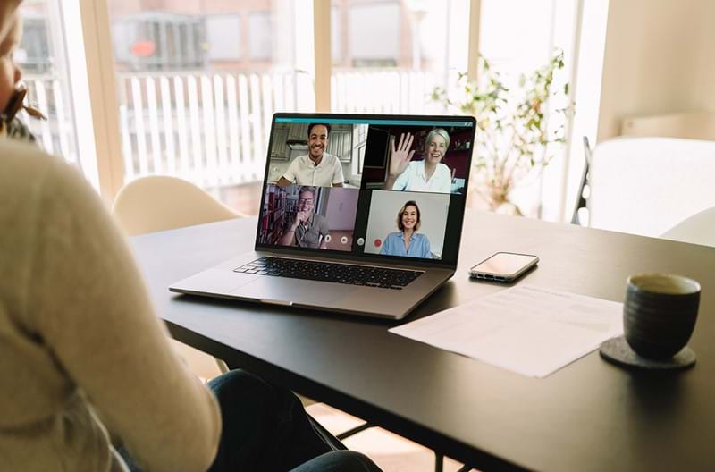 A person sitting at a table with their laptop open on a group video call.  