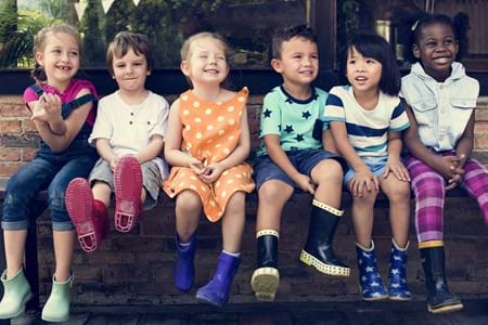 A group of young children sitting on a ledge wearing gum boots.