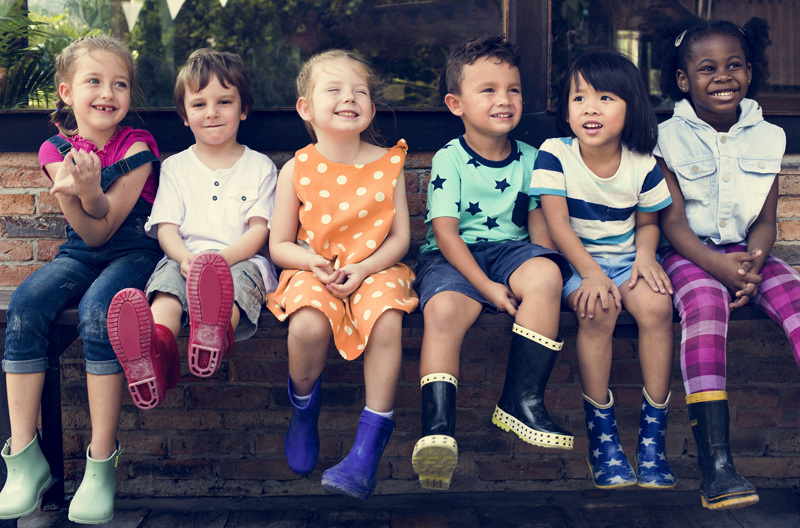 A group of young children sitting on a ledge wearing gum boots.