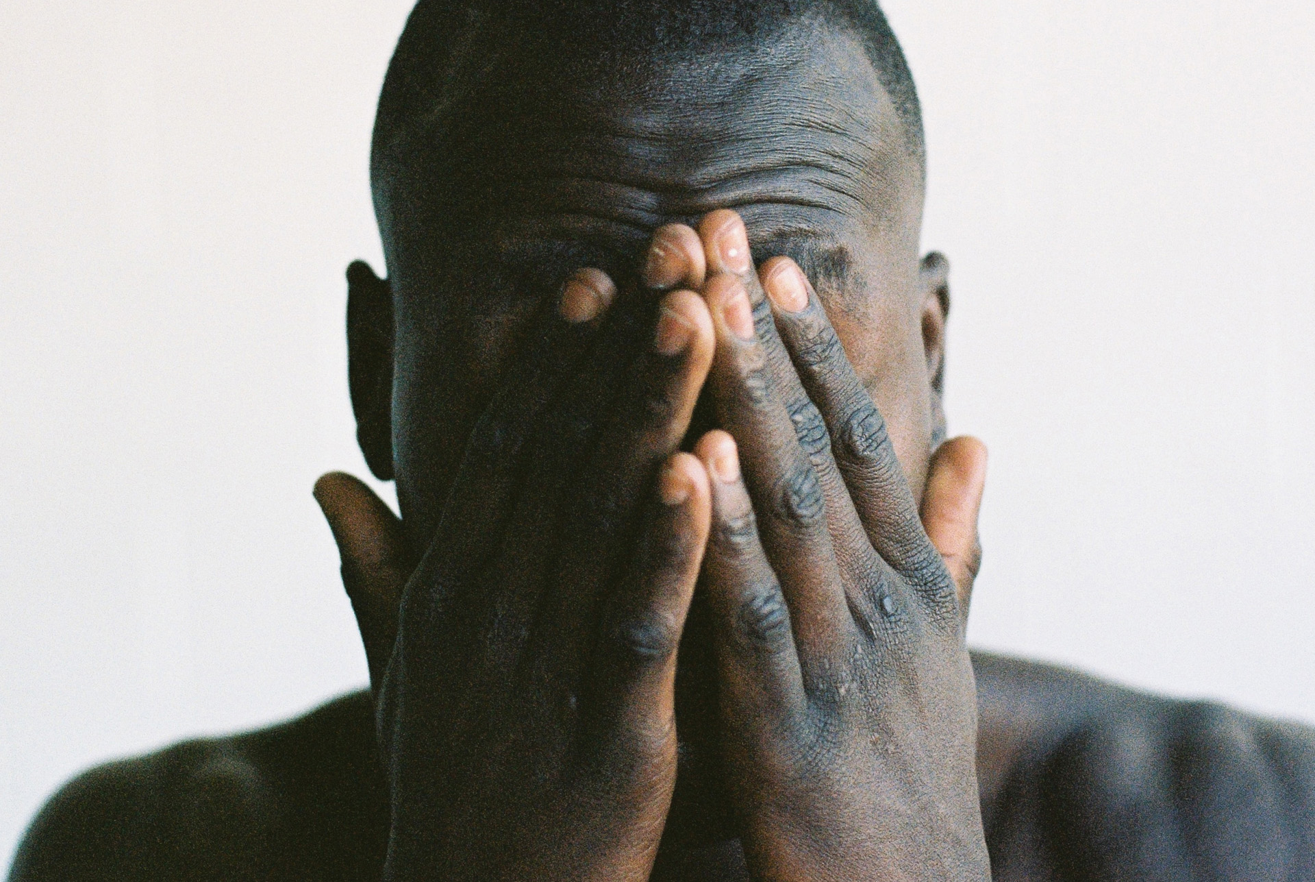 A shirtless man covering his face with his hands.