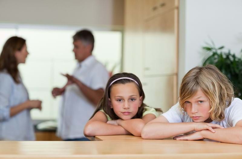 Two children unhappy with their parents arguing in the background. 